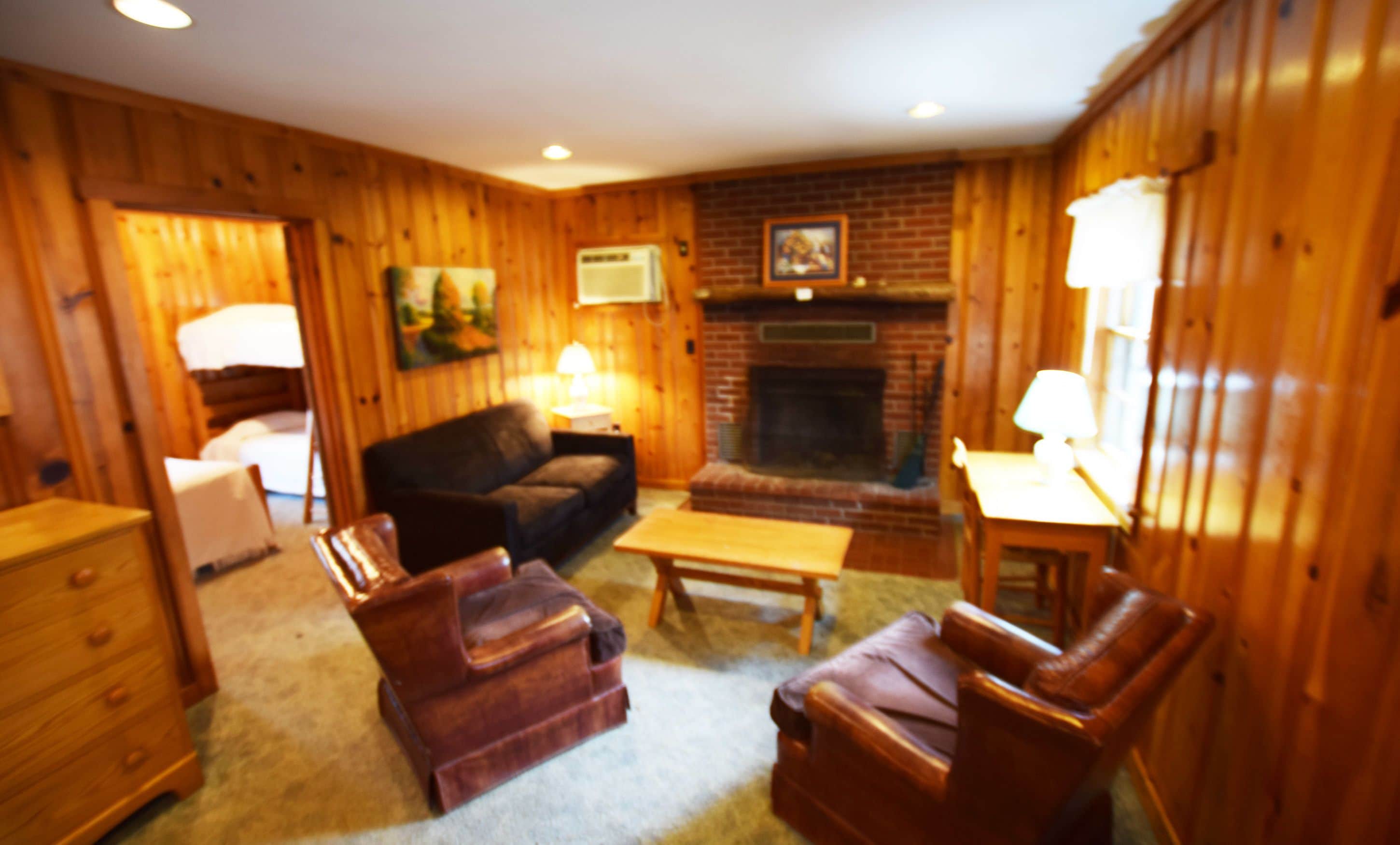 A cozy living room with wooden walls, a fireplace, a sofa, a coffee table, and a lamp.