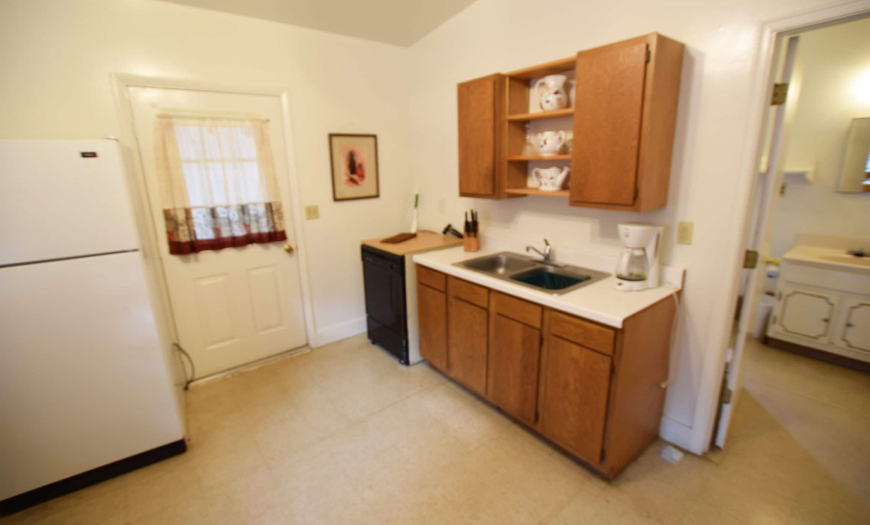 A compact kitchen with a white refrigerator, a sink, wooden cabinets, and a coffee maker.