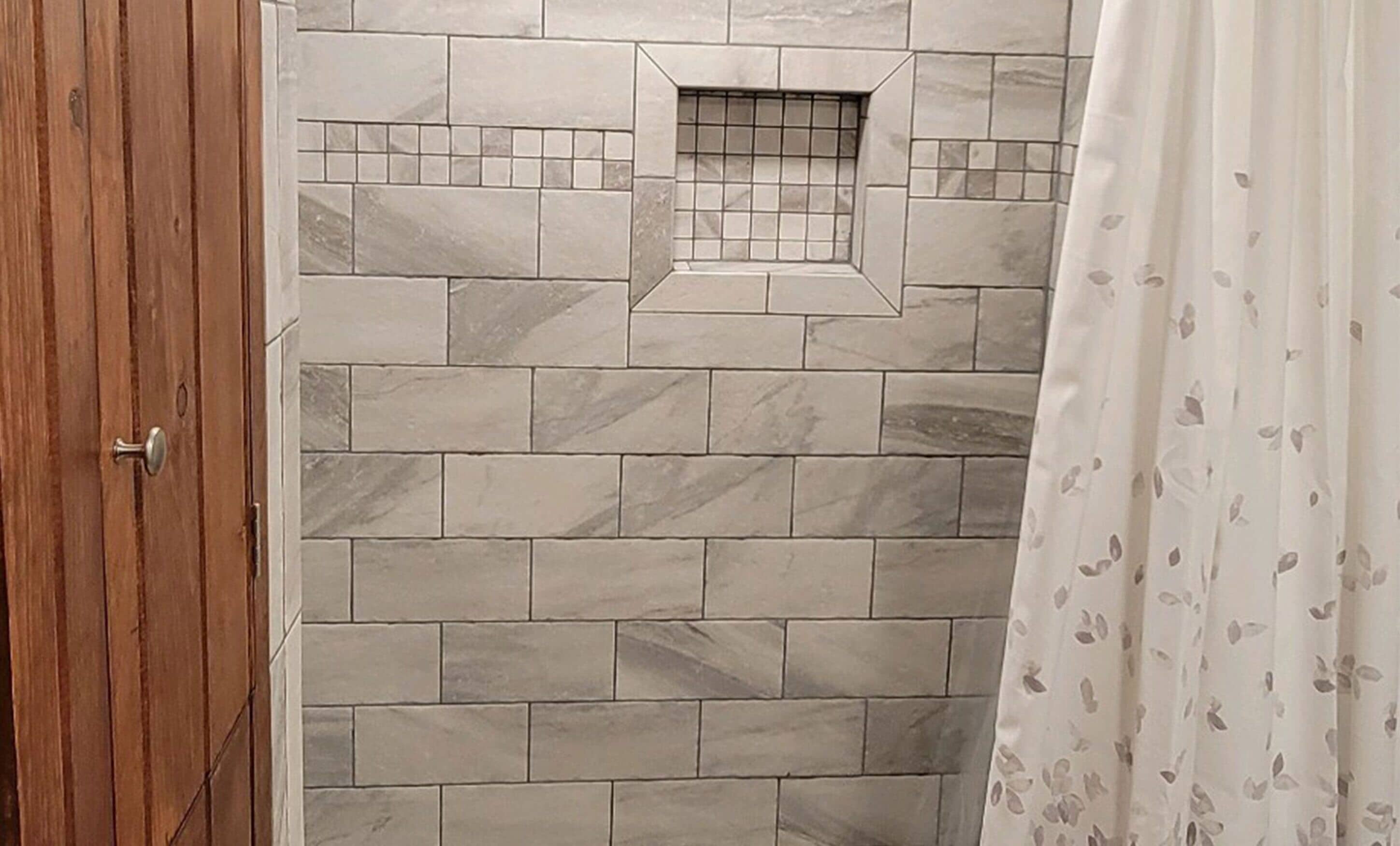 Une salle de bain avec un mur de douche carrelé et une porte en bois.