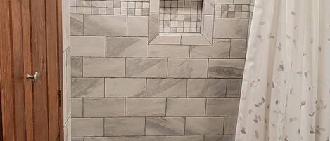 Une salle de bain avec un mur de douche carrelé et une porte en bois.