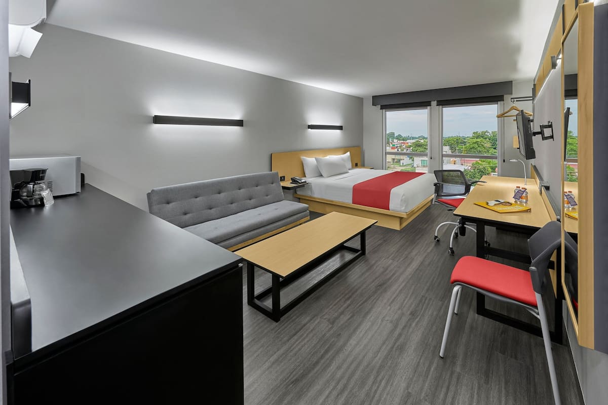 A modern hotel room with a bed, sofa, desk, and chair.