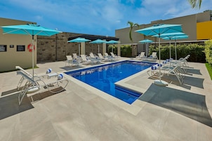 Una piscina al aire libre, sombrillas, sillones reclinables de piscina