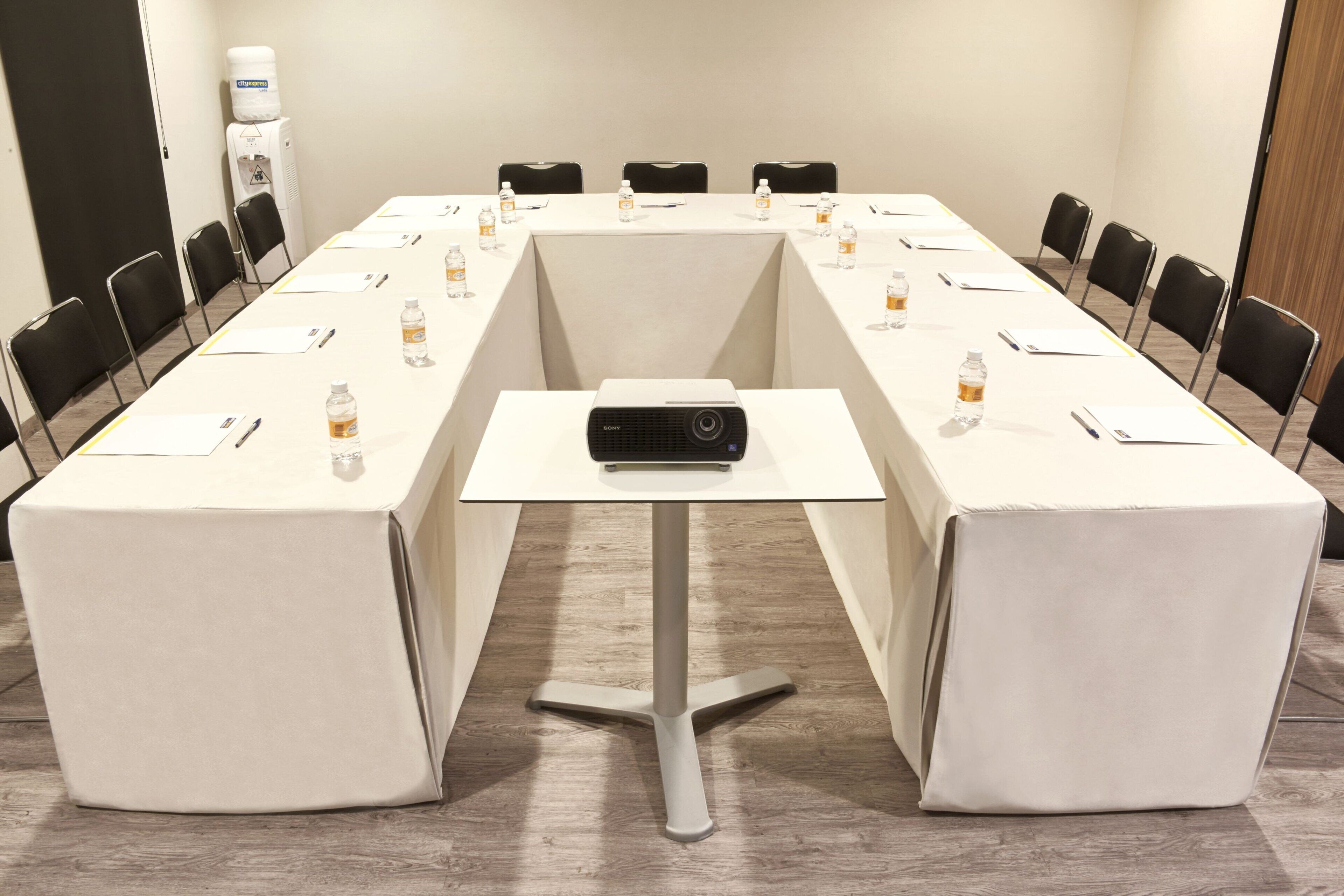 Un salón de conferencias con una mesa larga, sillas, un proyector y botellas de agua.