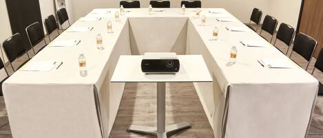 Un salón de conferencias con una mesa larga, sillas, un proyector y botellas de agua.