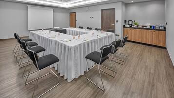 A conference room with a long table, chairs, a projector screen, and a kitchenette area.