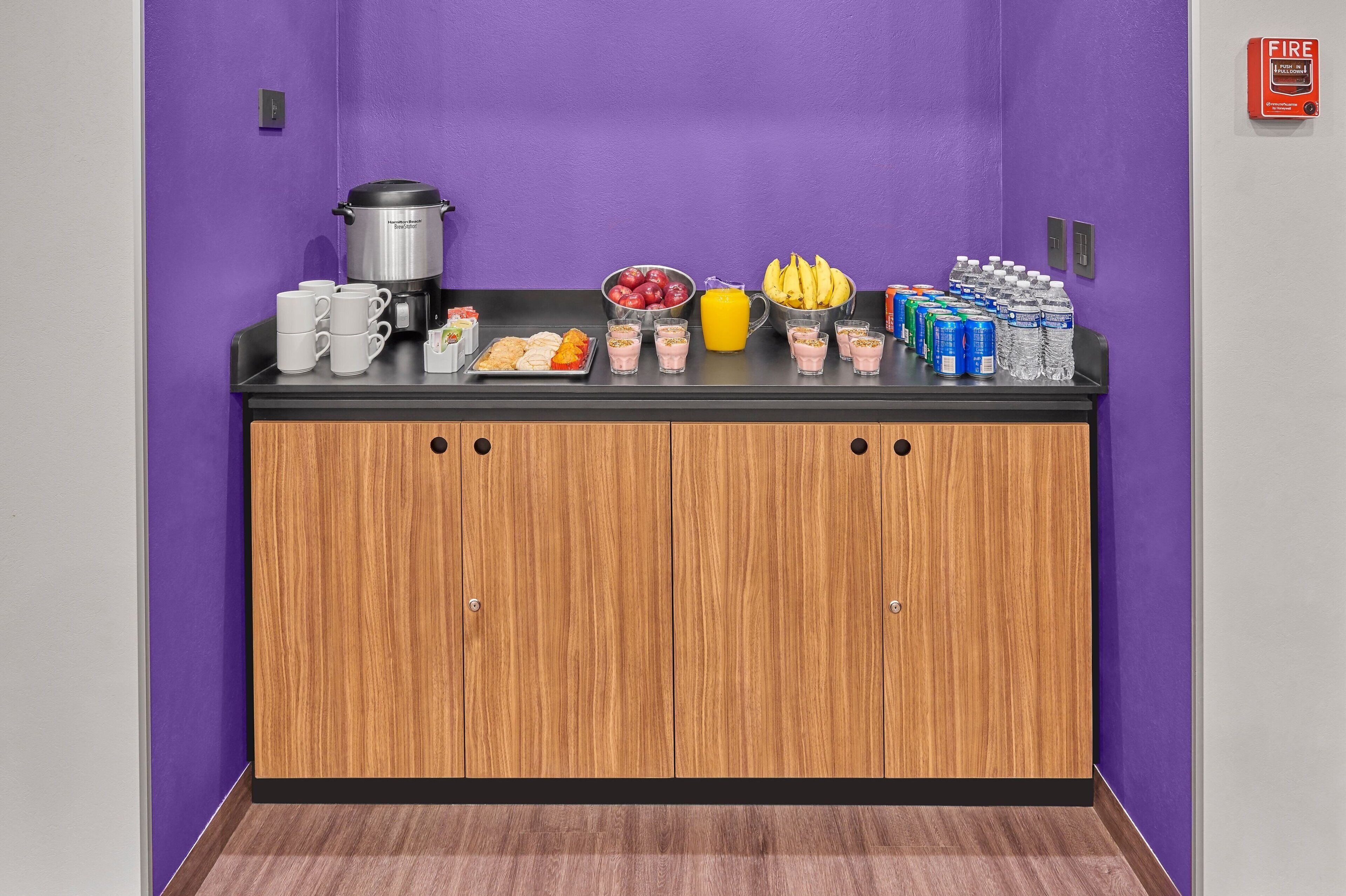 A breakfast bar with a coffee maker, fruit, and beverages.