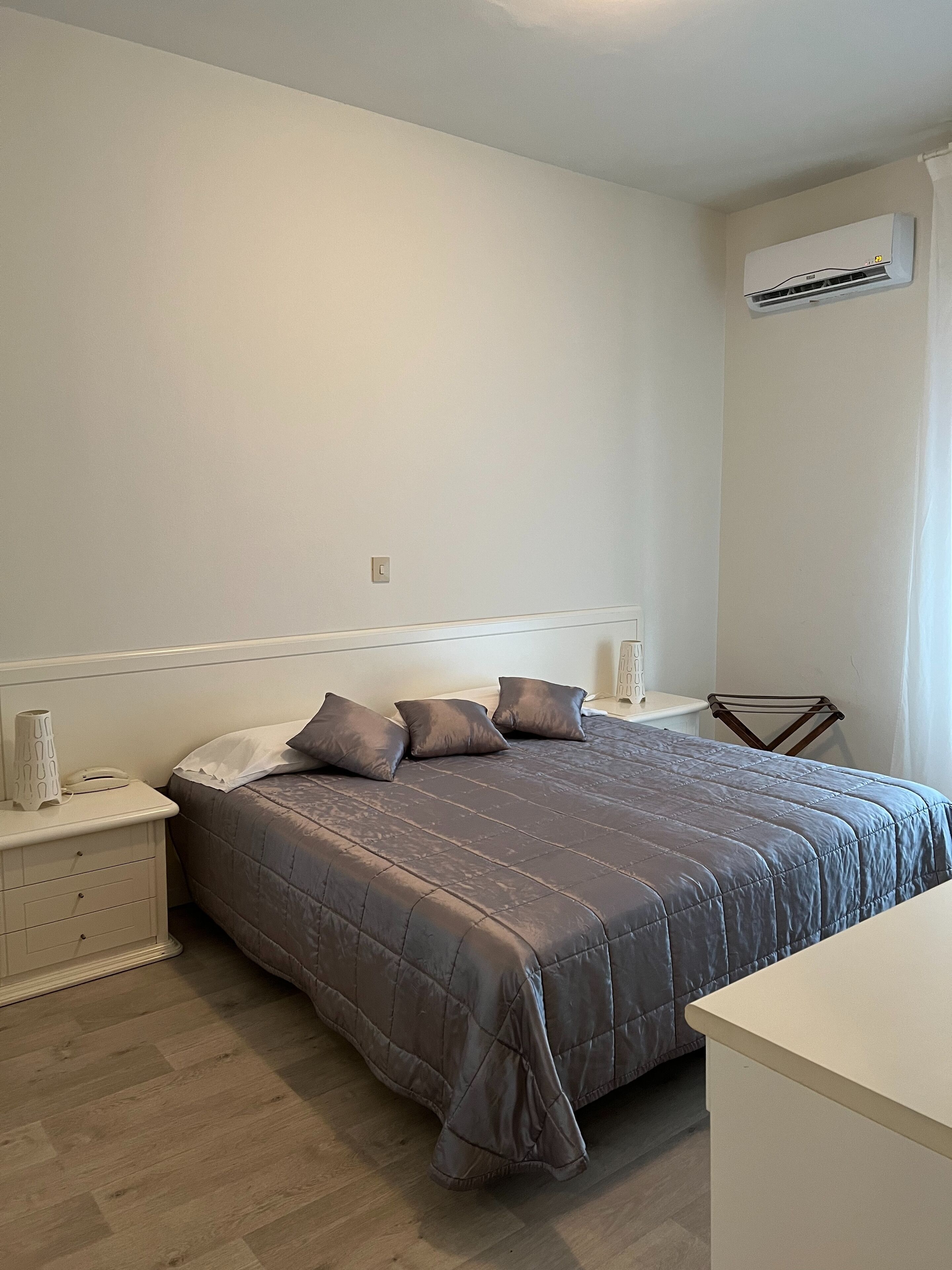 A bedroom with a bed, a nightstand, a bedside table, and an air conditioning unit on the wall.