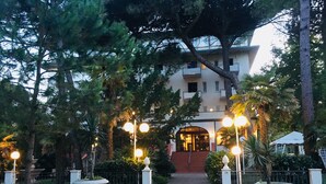 A building entrance with a paved pathway, surrounded by trees and potted plants. - Hotel Deanna Golf (Cervia)
