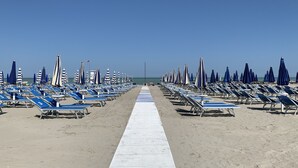 A beach with rows of sun loungers and umbrellas, a wooden walkway, and the ocean in the background. - Hotel Deanna Golf (Cervia)