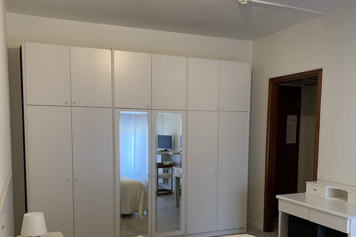 A bedroom with a large bed, white wardrobe, and a small desk.