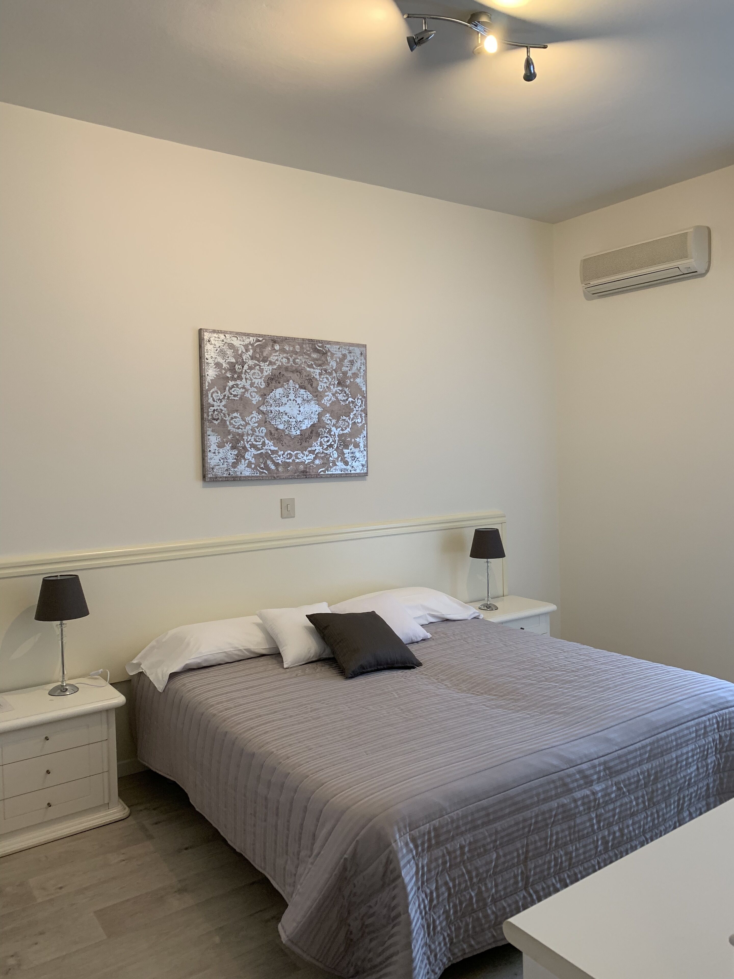 Een slaapkamer met een bed, twee nachtkastjes, een wandairconditioner en een plafondlamp.