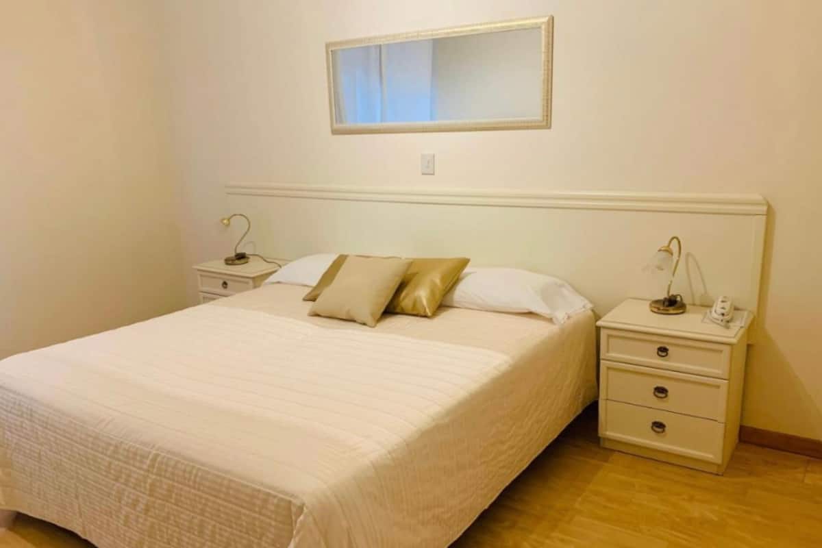 A neatly arranged bedroom with a large bed, two bedside tables, and a mirror on the wall.