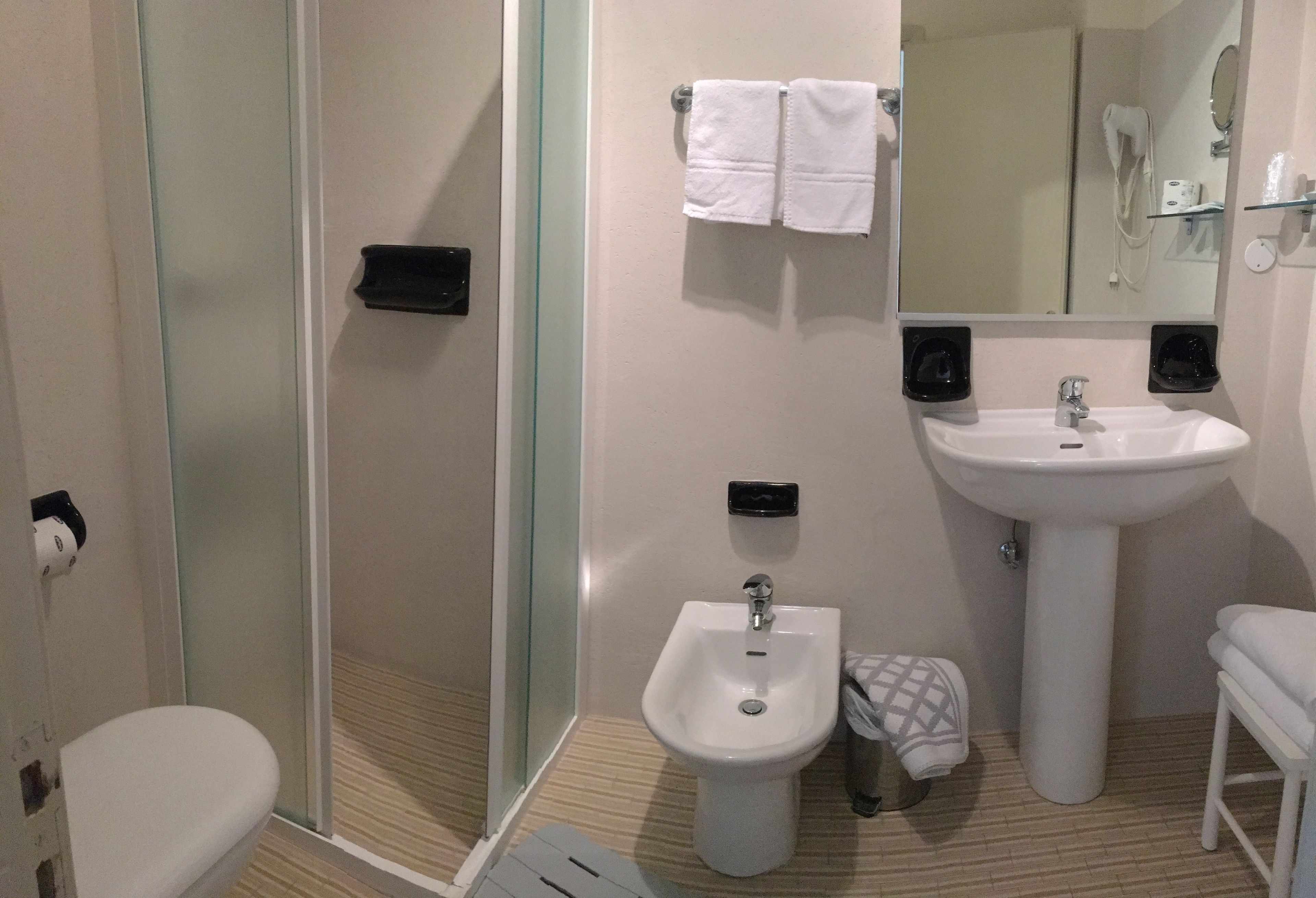 A bathroom with a glass-enclosed shower, a bidet, a sink, and a toilet.