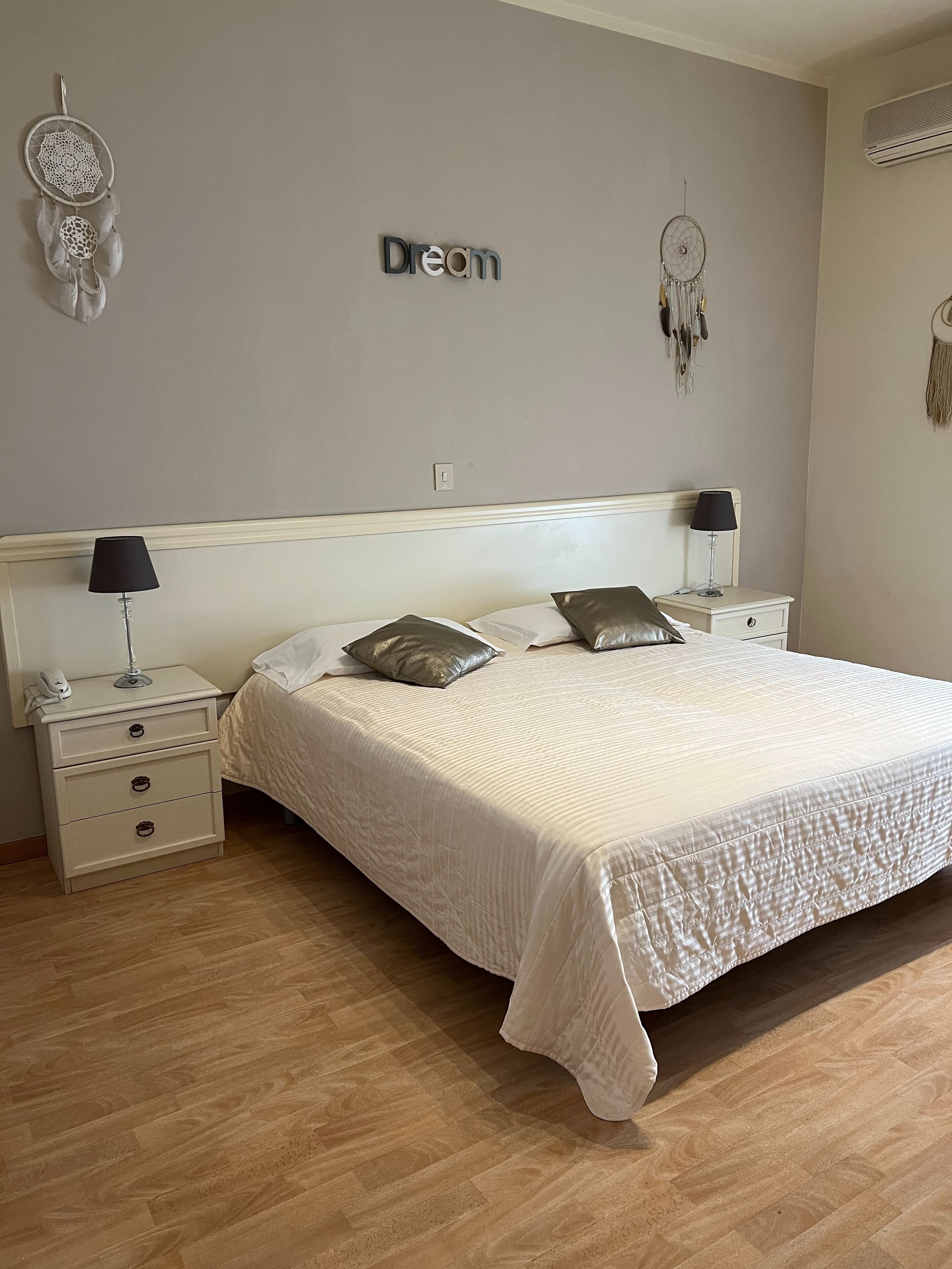 A bedroom with a large bed, two nightstands, a wall-mounted dreamcatcher, and a 'Dream' sign.