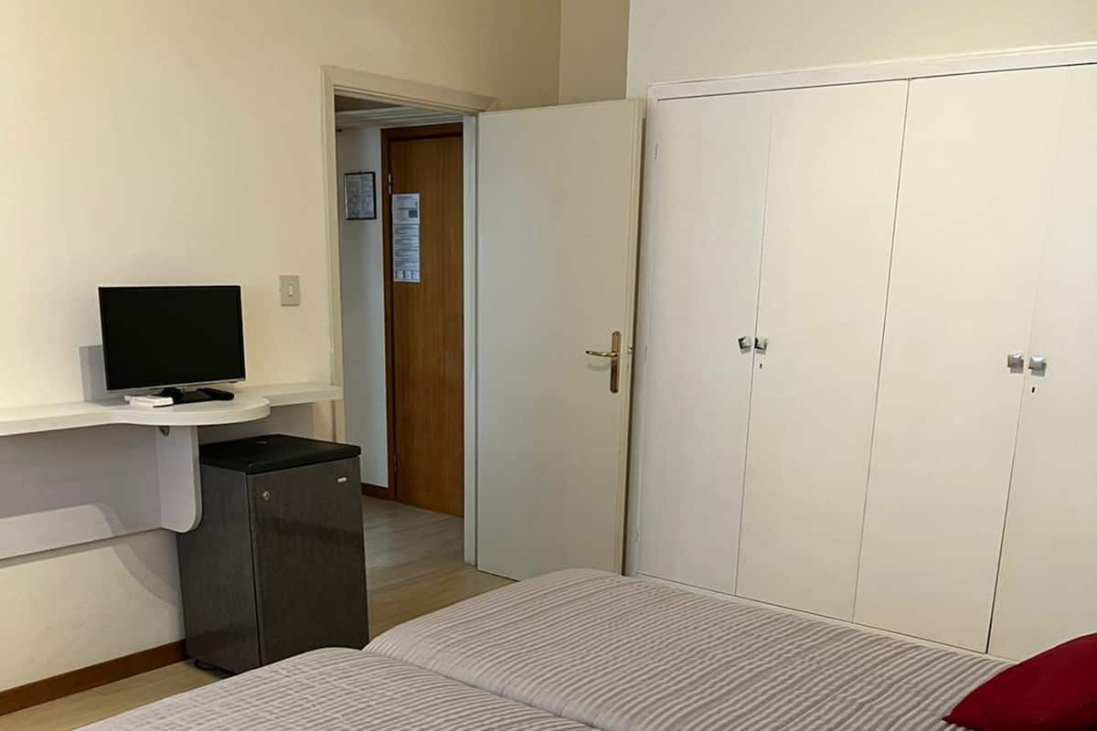 A bedroom with two beds, a desk with a computer, and a wardrobe.