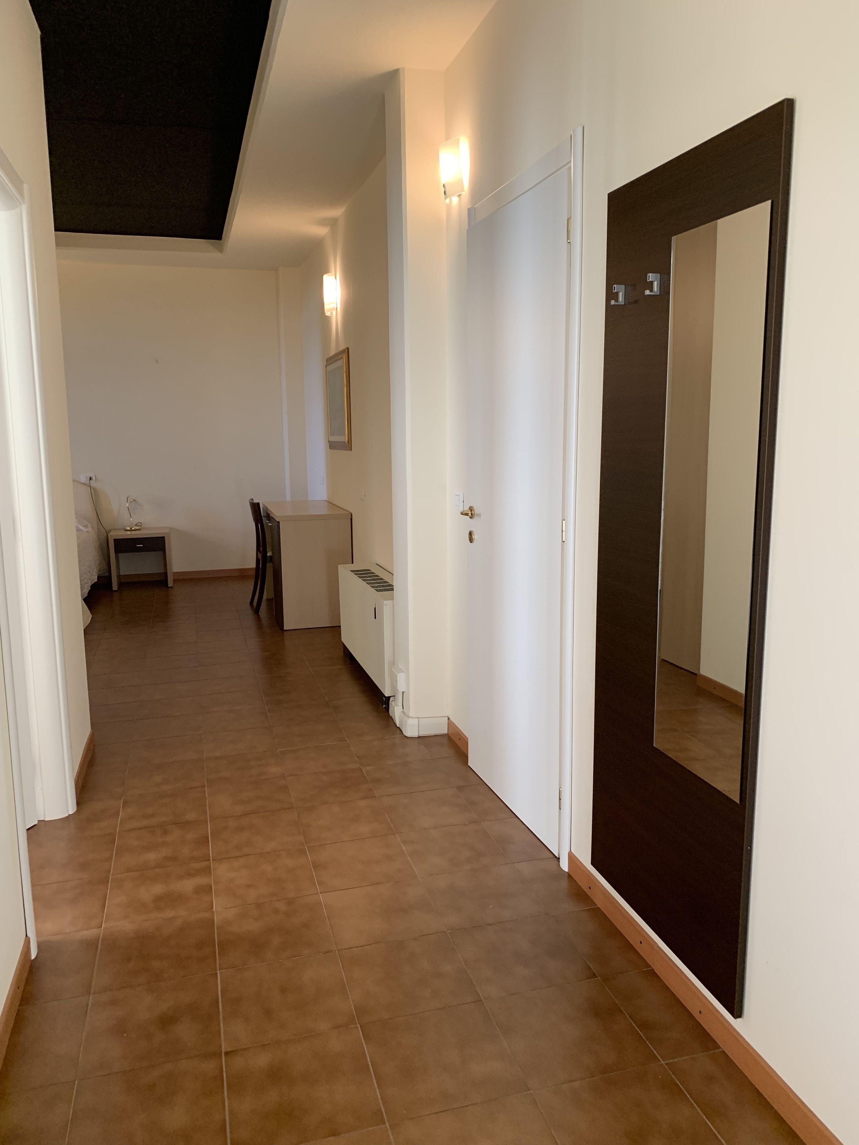 A hallway with a large mirror, a door, and a small seating area with a table and chairs.