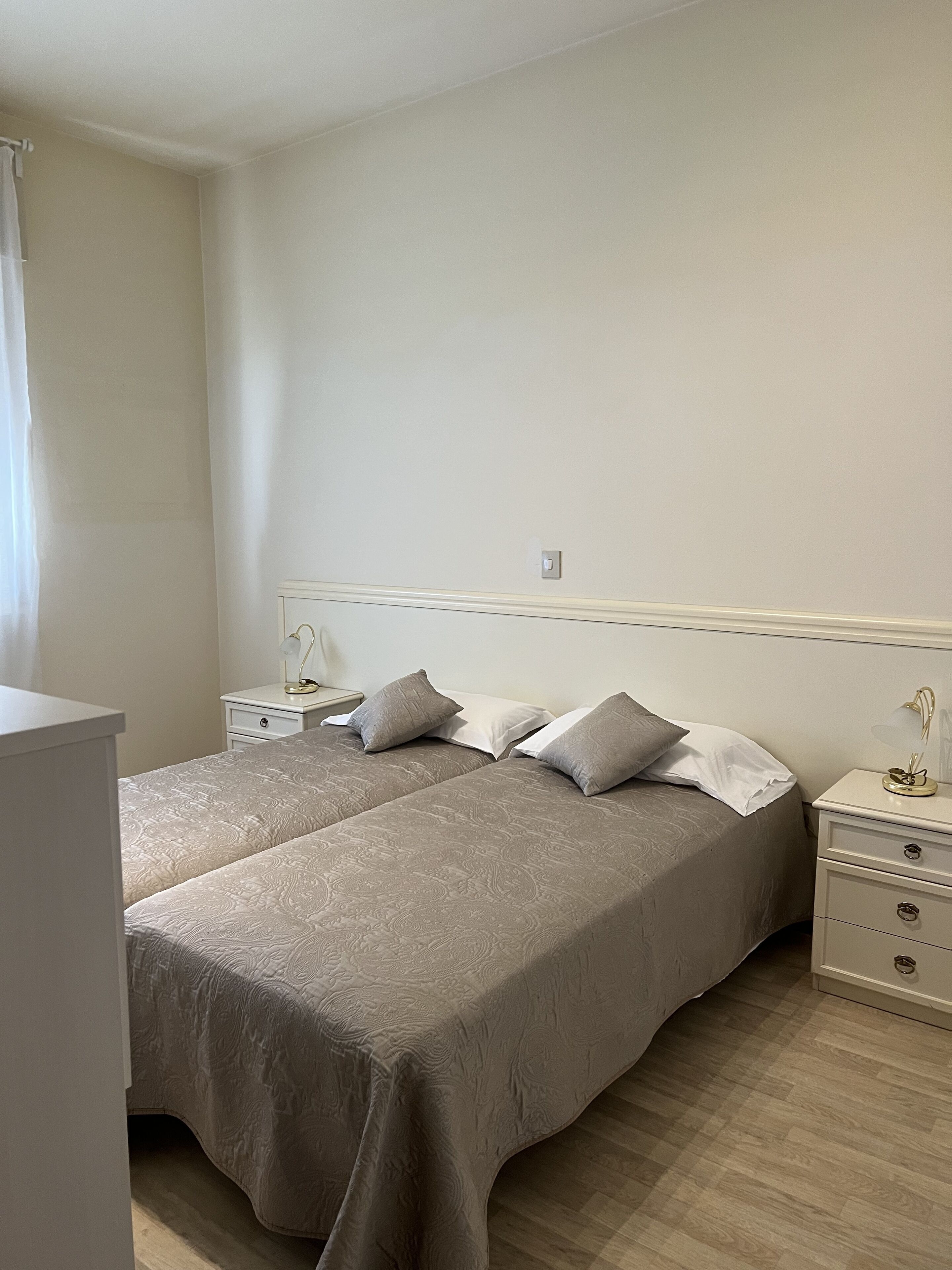 A bedroom with two beds, white nightstands, and a bedside table with a lamp.