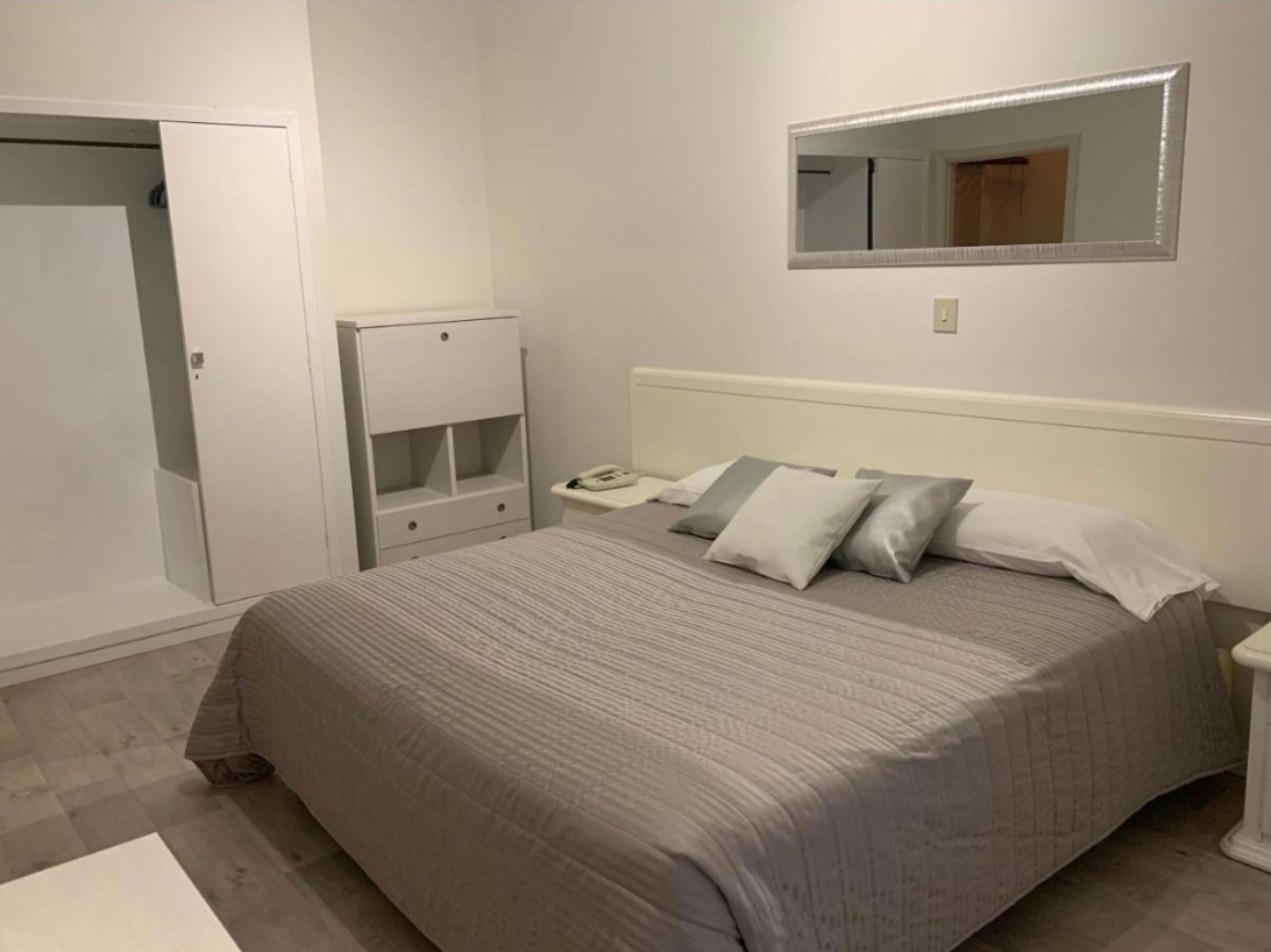 Un dormitorio con cama, mesita de noche y un espejo en la pared.