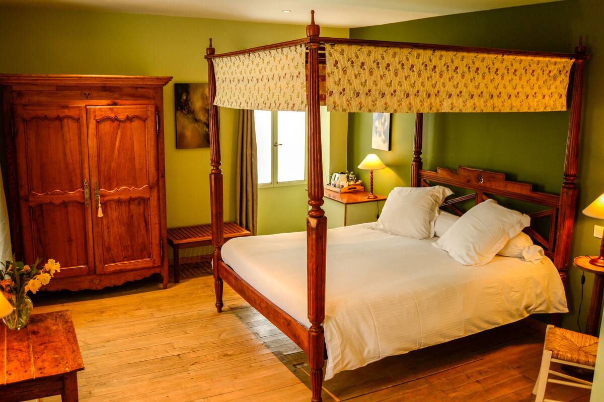 A four-poster bed with a canopy, a wooden wardrobe, a bedside table with a lamp, and a small chair.