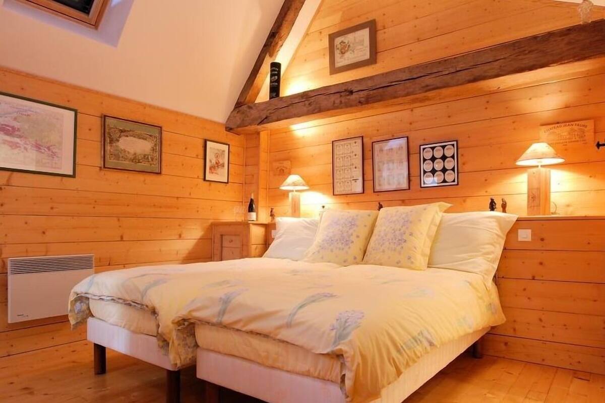 A cozy wooden room with a large bed, framed pictures on the walls, and a ceiling with exposed beams.