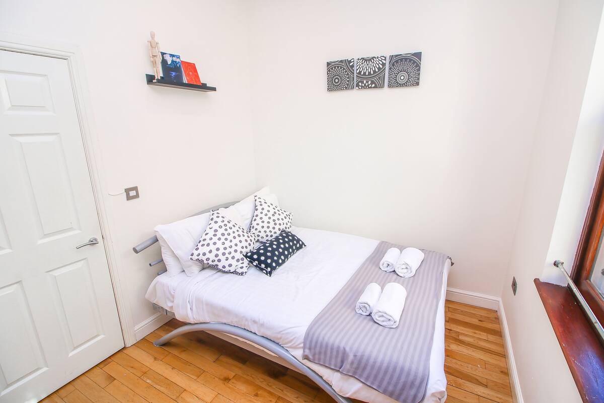 A neatly made bed with a grey and white striped blanket, a wooden headboard, and a wooden floor.