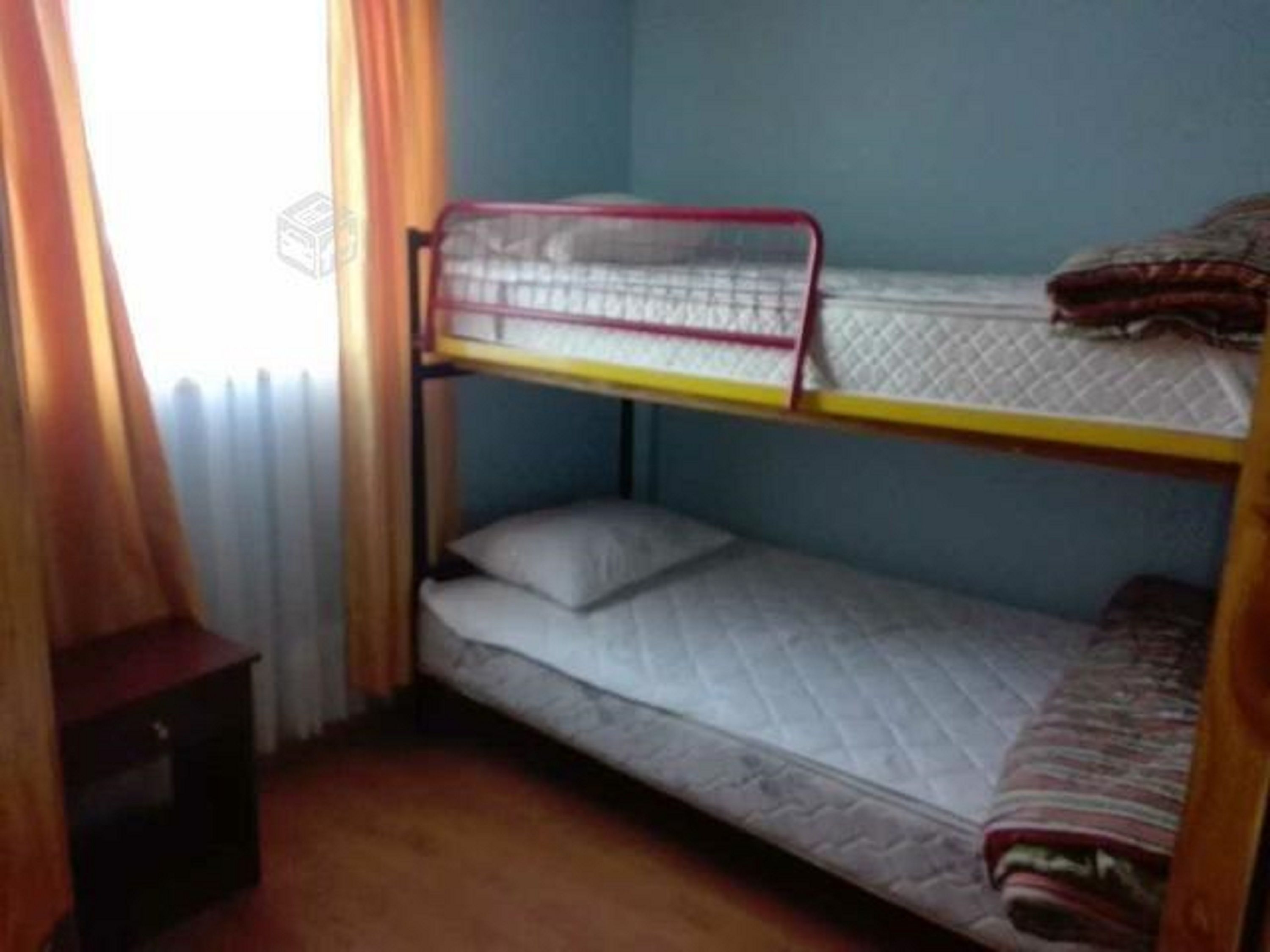 Habitación con literas, piso de madera, una mesita pequeña y una ventana con cortinas.