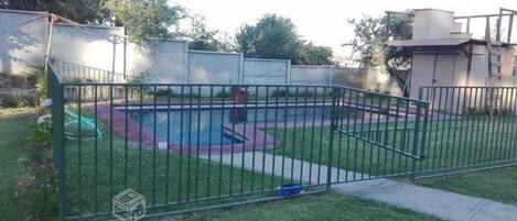 A fenced backyard with a pool, a grassy area, and a paved walkway.
