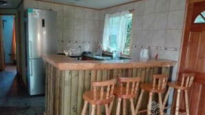 Una cocina con barra de madera, un refrigerador y una ventana con cortina.