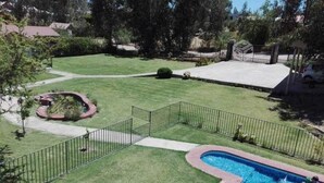 Un patio trasero con piscina, área de juegos cercada y césped bien cuidado.
