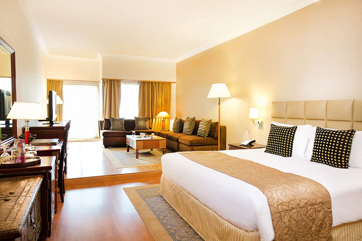 Ein Hotelzimmer mit einem großen Bett, einem Schreibtisch mit Lampe, einer Couch und einem Fernseher.