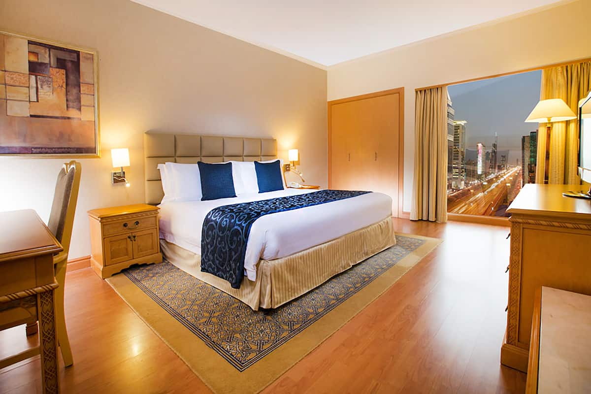 Une chambre d’hôtel avec un grand lit, une table de chevet, un bureau et une vue sur le paysage urbain par la fenêtre.