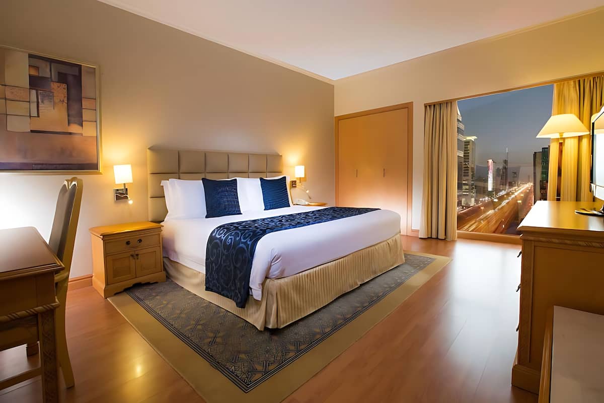 Une chambre d’hôtel avec un grand lit, des lampes de chevet, un bureau et une vue sur le paysage urbain par la fenêtre.
