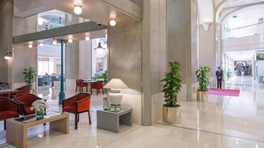 Un vestíbulo amplio con mobiliario moderno, que incluye una recepción, zona de estar y plantas en macetas.