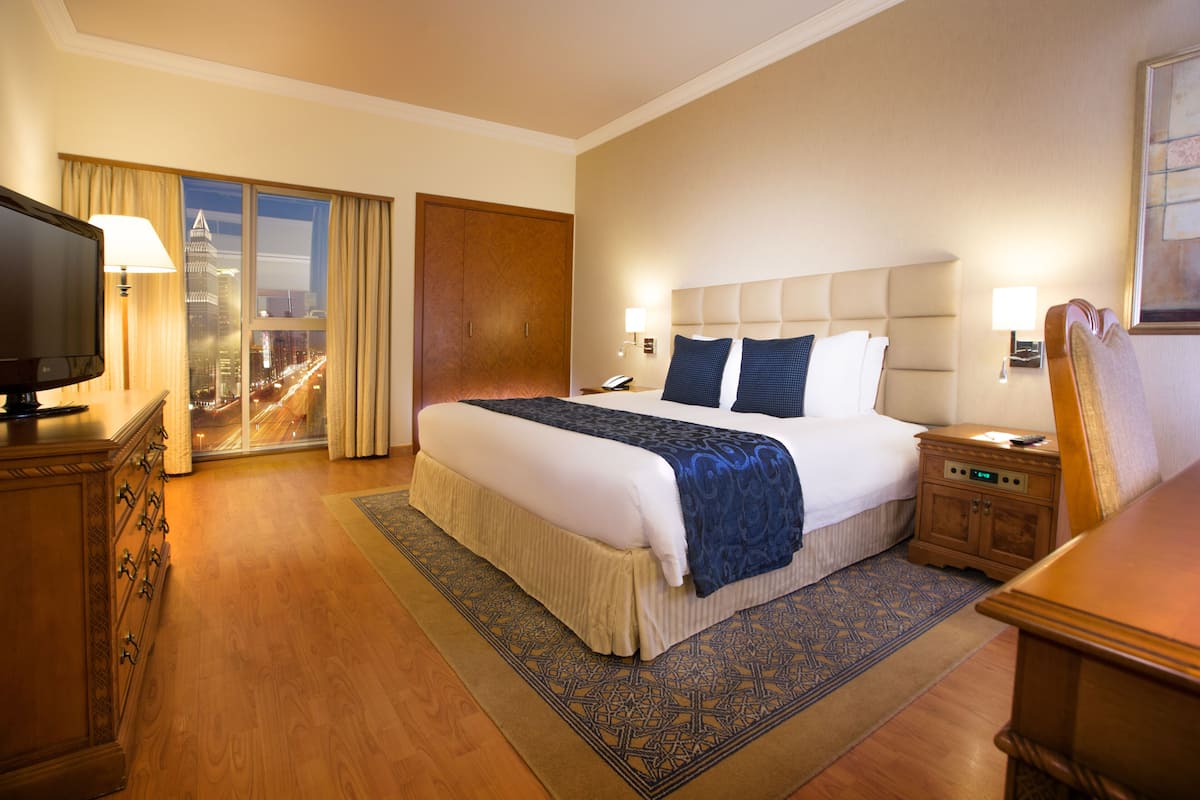 Une chambre d’hôtel avec un grand lit, une télévision, une table de chevet et une vue sur le paysage urbain par la fenêtre.