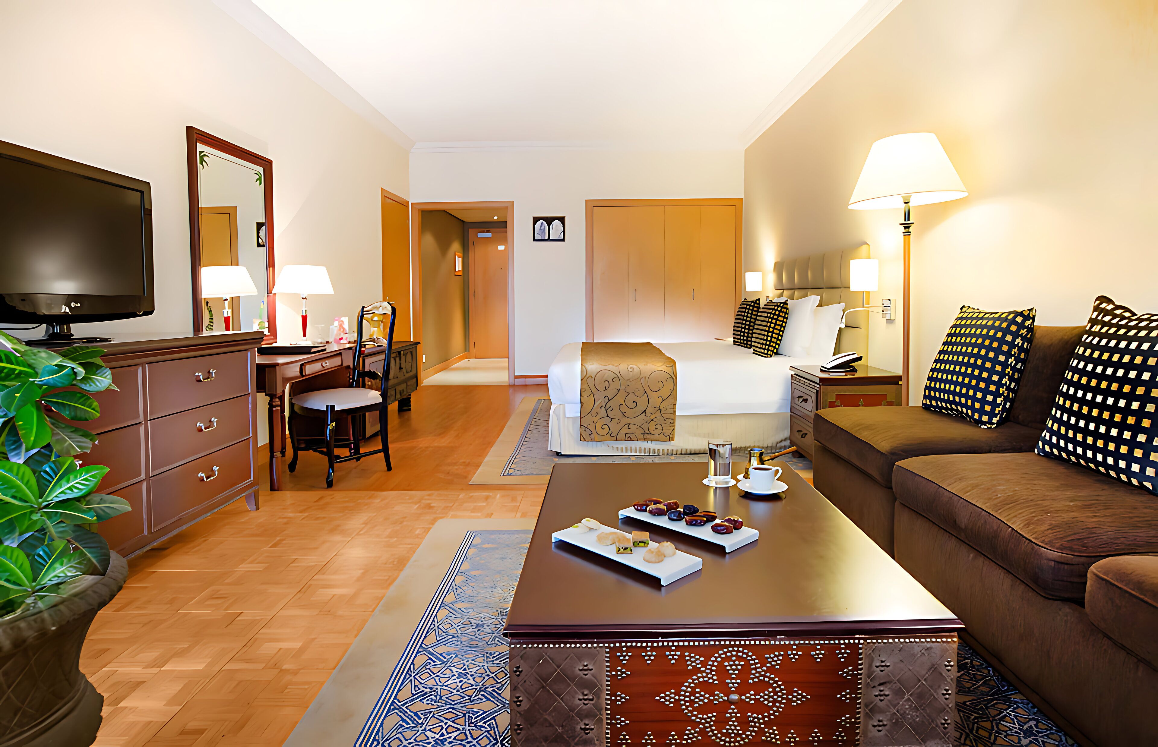 A hotel room with a bed, a sofa, a TV, a desk, and a coffee table with pastries.