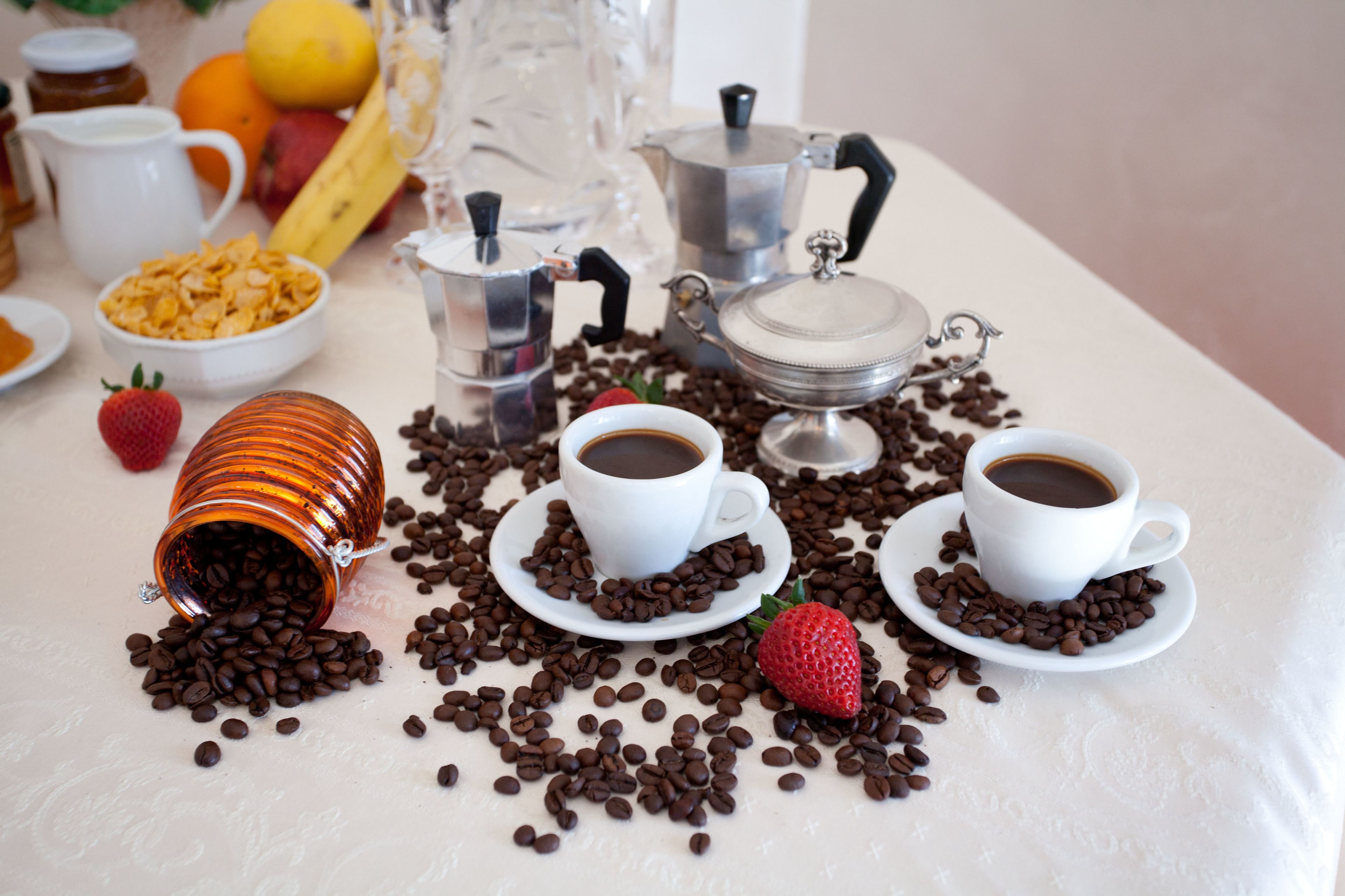 A table with coffee cups, a coffee pot, a jar of sugar, and scattered coffee beans.