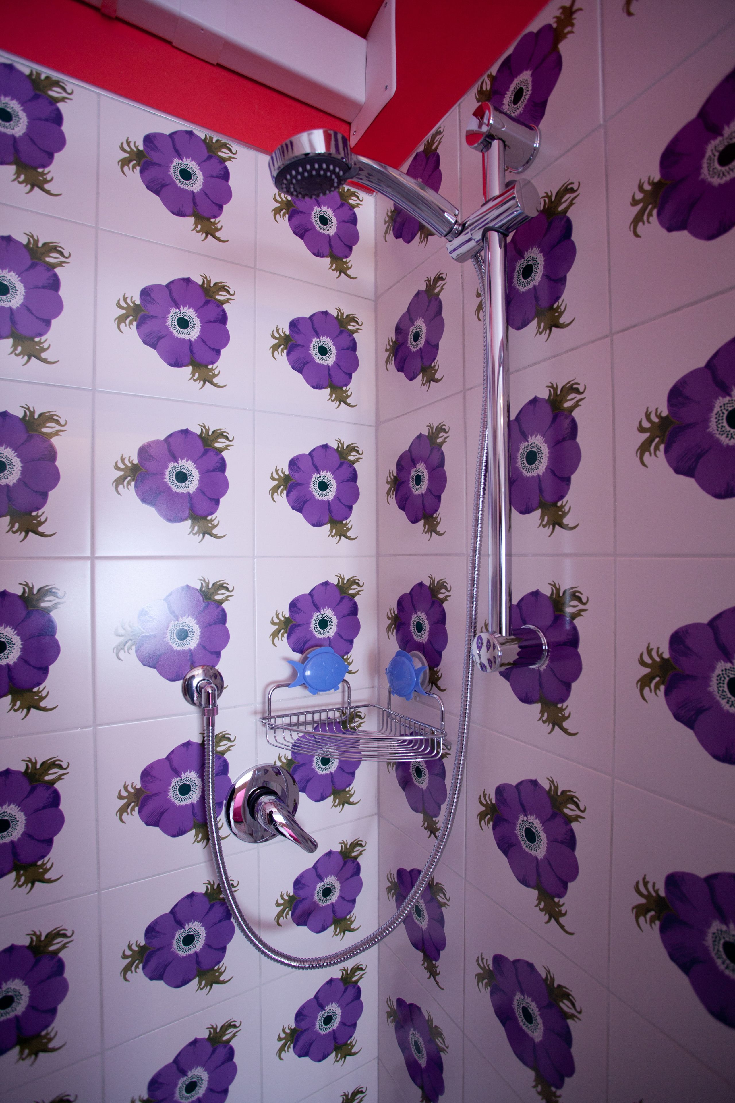 Een douche met een paars bloemmotief op de wand, een chroomdouchekop en een handdouche.
