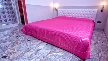 A room with a bed, marble floor, and two wall sconces.