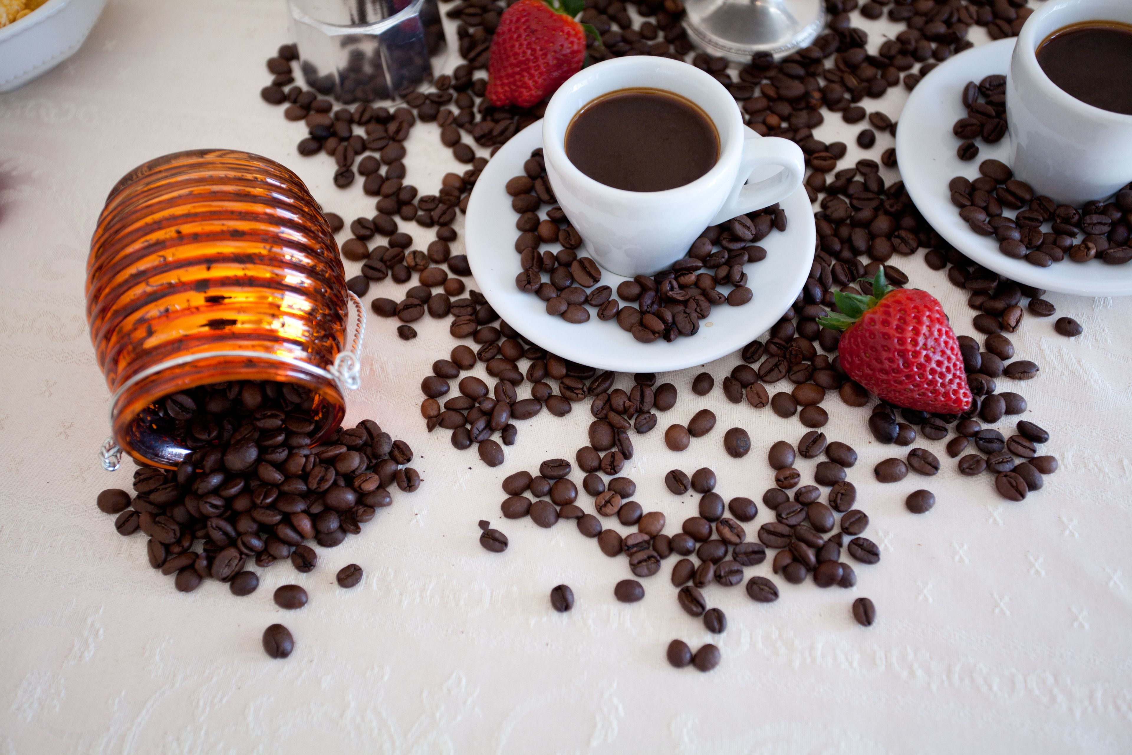Taula amb grans de cafè, tasses de cafè i una fresa.