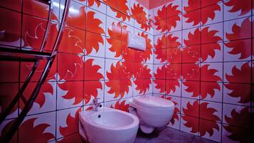 A bathroom with red and white patterned tiles, two white bidets, and a hand dryer.