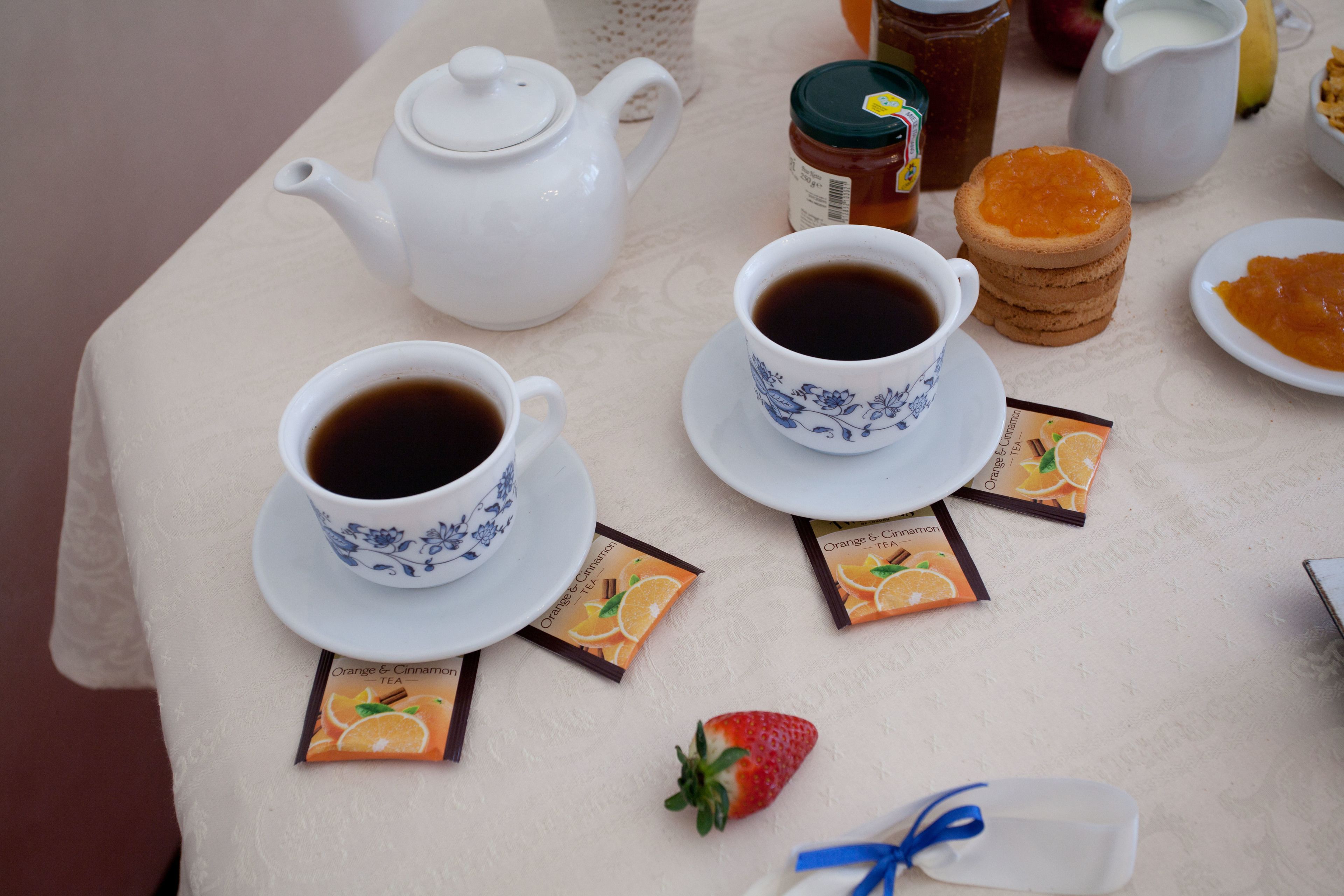 A table set with two cups of black tea, a teapot, a jar of honey, a plate of toast, and a small strawberry.