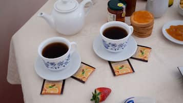 A table set with two cups of black tea, a teapot, a jar of honey, a plate of toast, and a small strawberry.