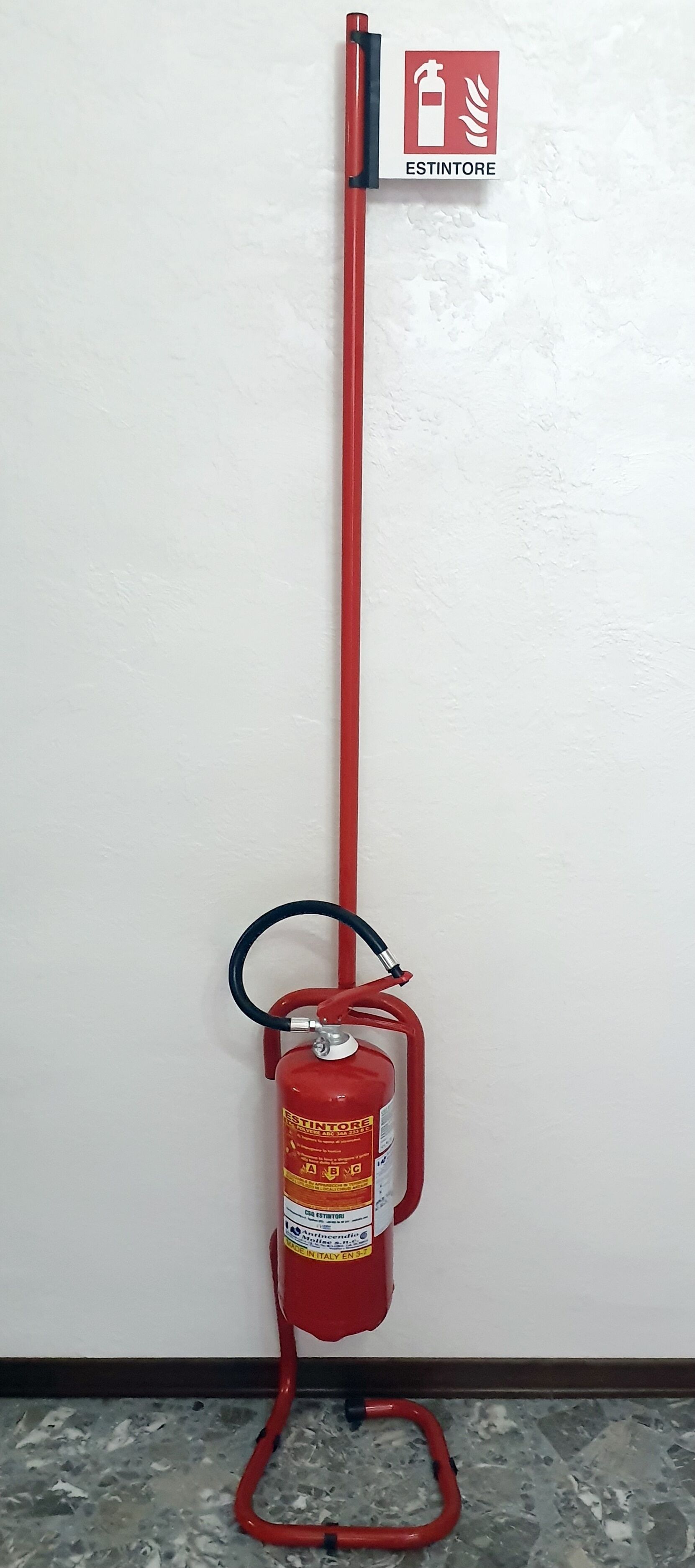 Extintor rojo montado en la pared con una manguera conectada.