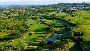 Vista aérea de un campo de golf con múltiples áreas verdes, peligros de agua y una zona residencial circundante.