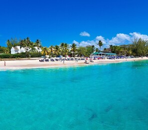 A beach with clear turquoise water, palm trees, and beach umbrellas. - Sweet Spot (Westmoreland)
