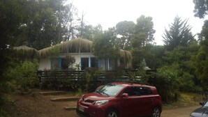 A red car parked in front of a building with a thatched roof, surrounded by trees. - 440 Cachagua (Zapallar)