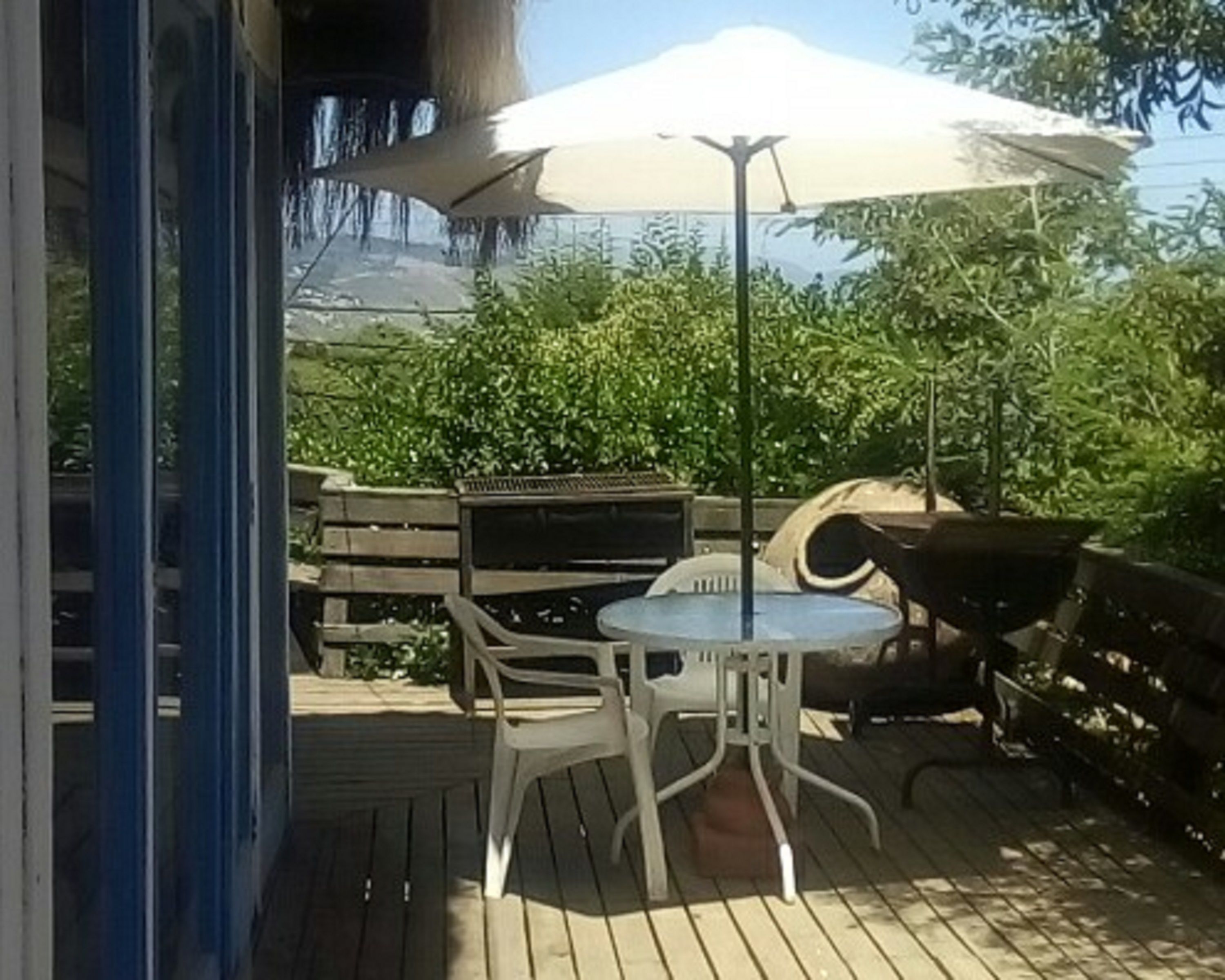 An outdoor patio with a wooden deck, a round table with chairs, a large umbrella, and a grill.