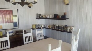 A dining area with a white table and chairs, a chandelier, and shelves with kitchenware. - 440 Cachagua (Zapallar)