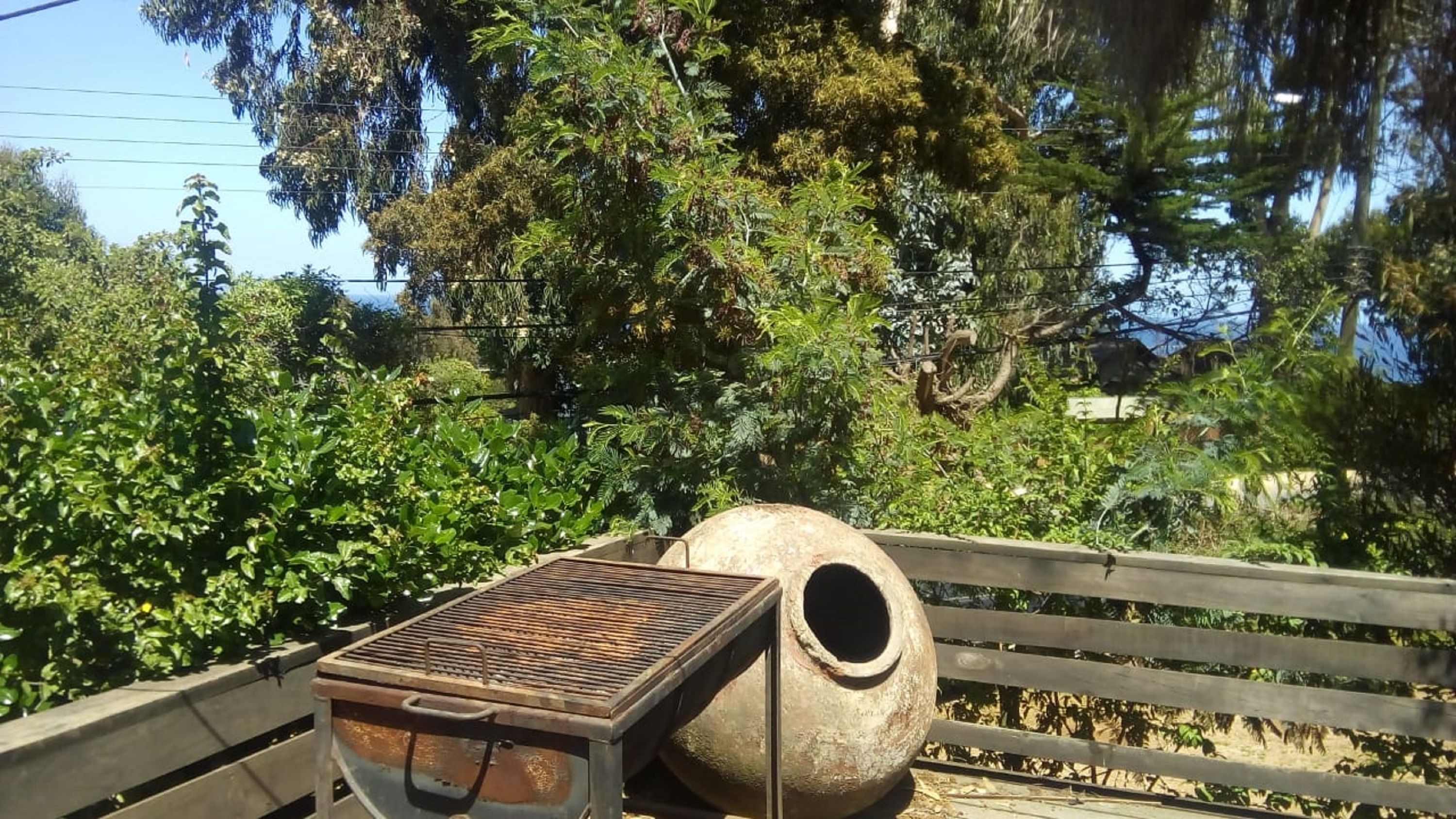 A rustic outdoor setting with a metal grill and a large clay pot on a wooden bench.