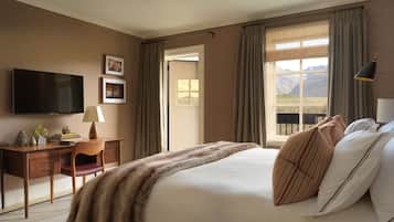 Une chambre d’hôtel avec un grand lit, un bureau avec une lampe, une télévision et une fenêtre avec des rideaux.